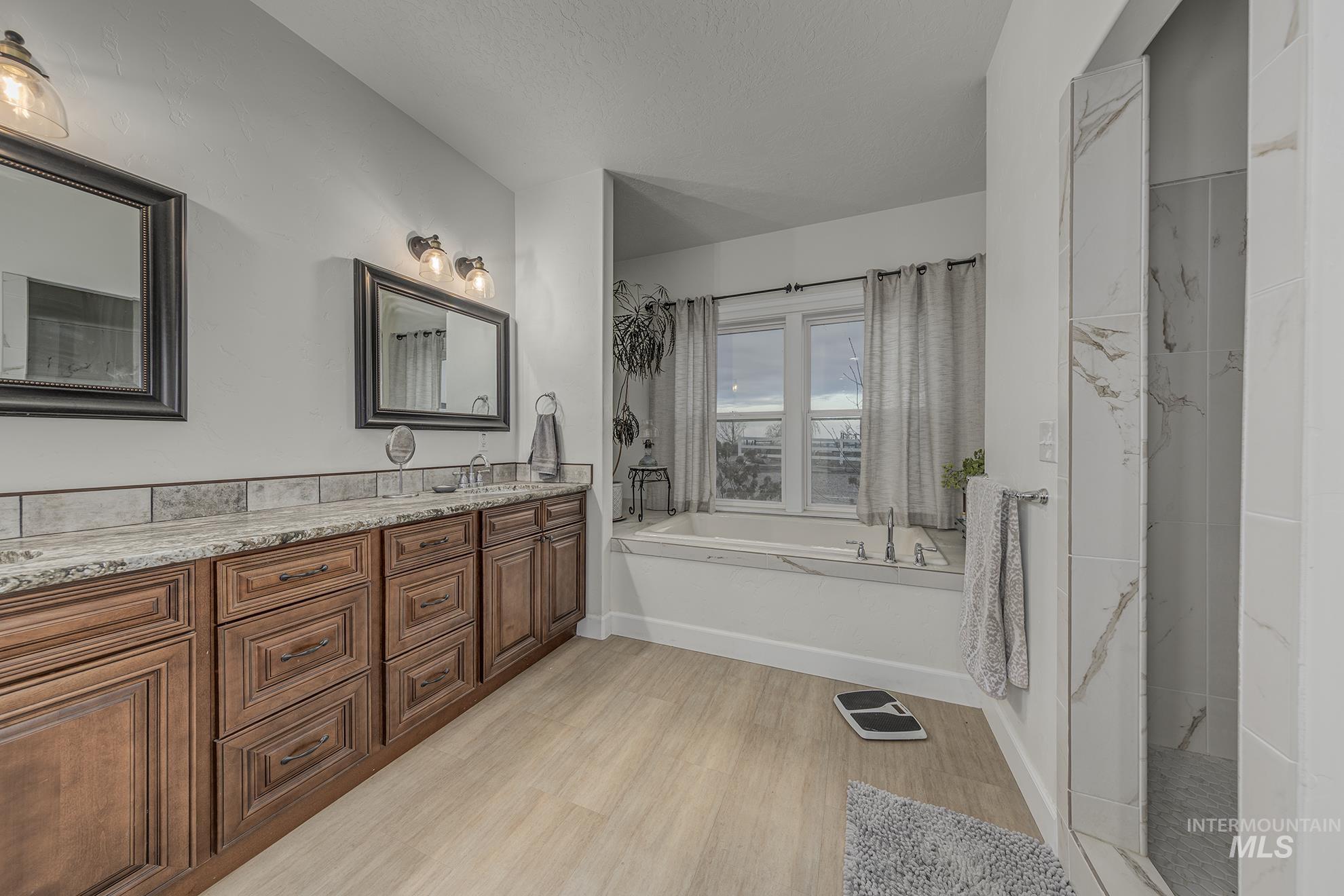 Full bath with double vanity, light wood-style flooring, and a bath