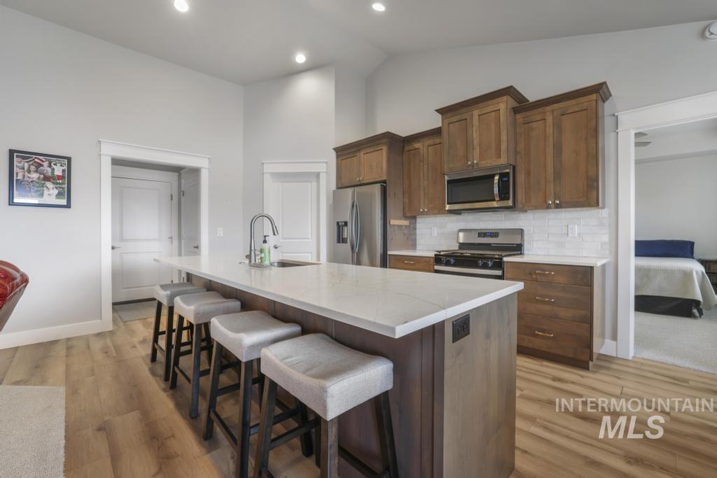 Kitchen featuring a kitchen island with sink, stainless steel appliances, light wood-type flooring, a kitchen breakfast bar, and recessed lighting