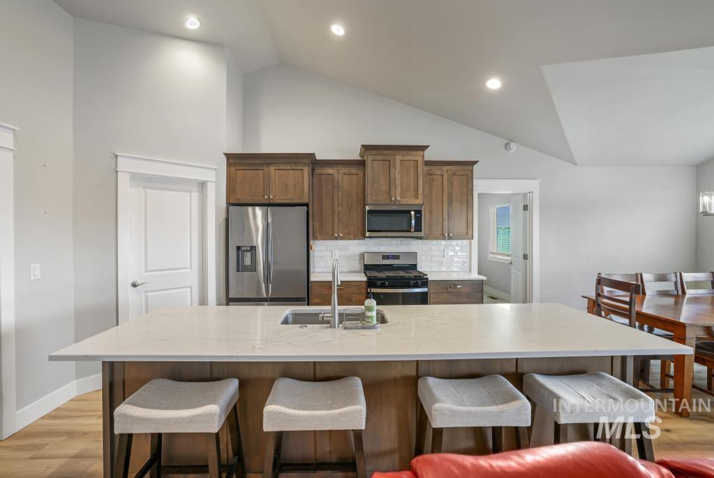Kitchen with light wood-style floors, appliances with stainless steel finishes, a breakfast bar area, light stone countertops, and recessed lighting