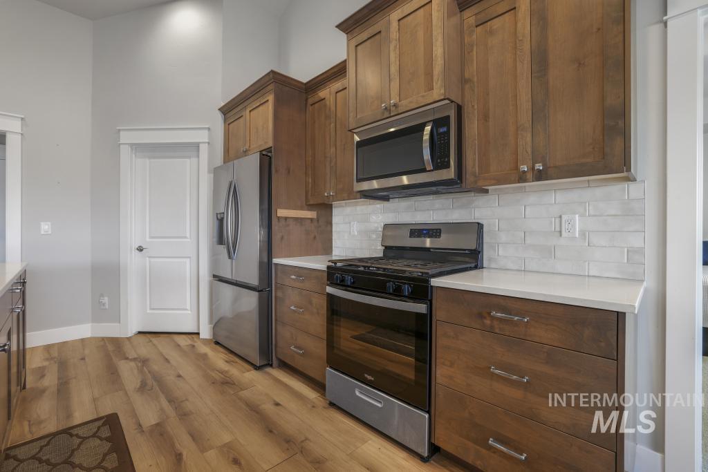 Kitchen featuring stainless steel appliances, light wood-style floors, decorative backsplash, brown cabinetry, and light stone counters
