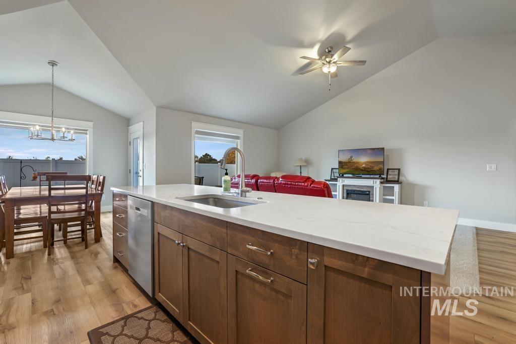 Kitchen with lofted ceiling, pendant lighting, an island with sink, open floor plan, and light wood-type flooring