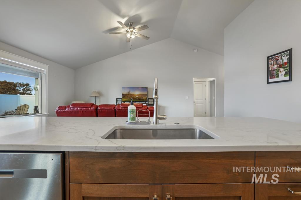 Kitchen featuring brown cabinets, light stone countertops, lofted ceiling, dishwasher, and a ceiling fan