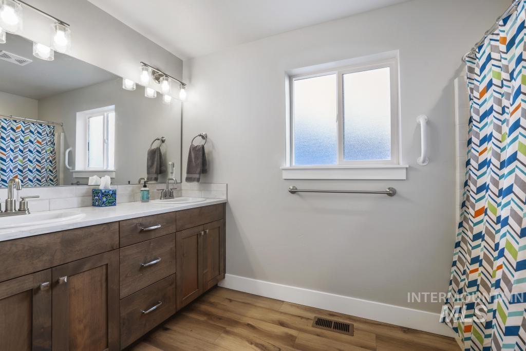 Full bathroom featuring curtained shower, double vanity, and light wood-style floors