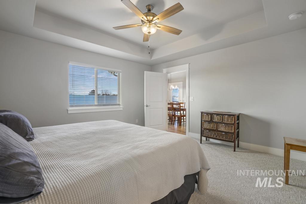 Carpeted bedroom featuring a raised ceiling and a ceiling fan