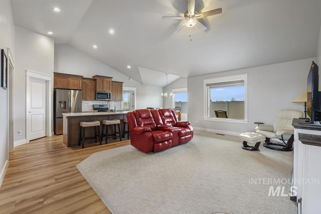 Living area featuring a ceiling fan, light wood-style flooring, recessed lighting, high vaulted ceiling, and a chandelier