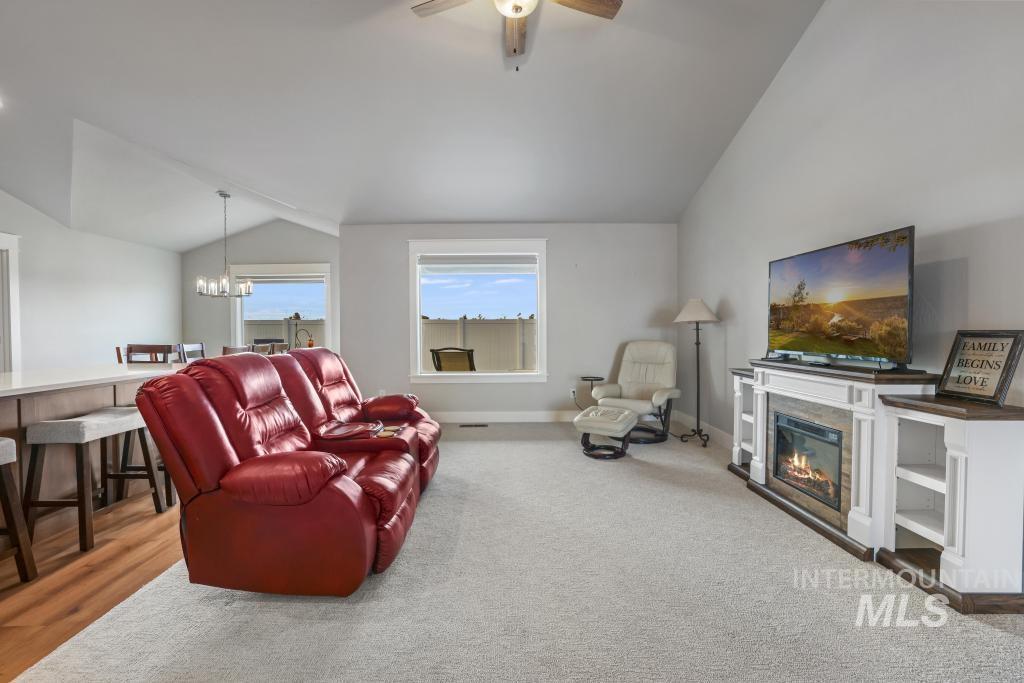 Living area with vaulted ceiling, a glass covered fireplace, a chandelier, light carpet, and a ceiling fan