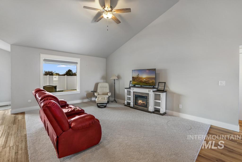 Living room with lofted ceiling, a glass covered fireplace, ceiling fan, and light wood-style floors
