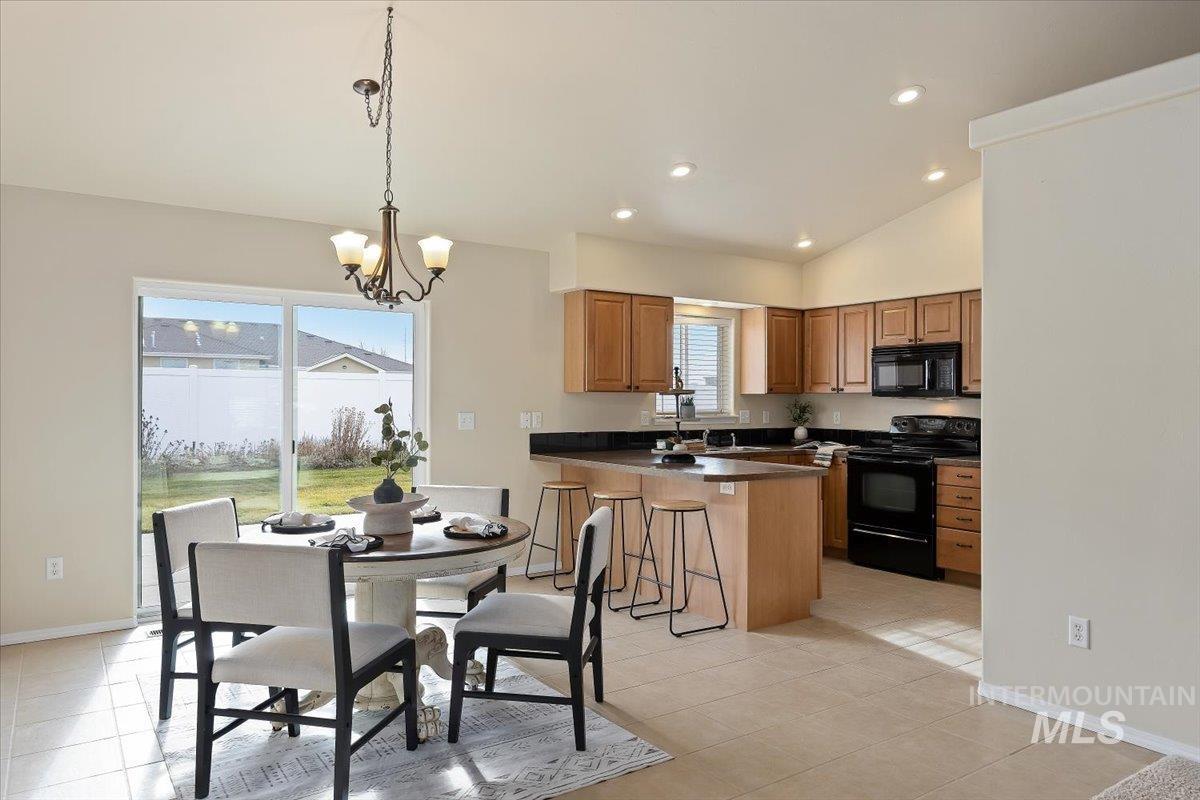Kitchen featuring black appliances, pendant lighting, a breakfast bar area, brown cabinets, and light tile patterned flooring