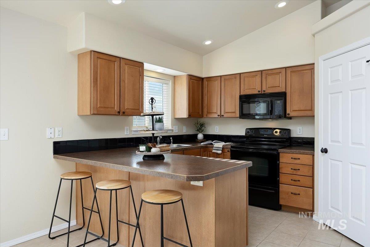 Kitchen featuring black appliances, a breakfast bar area, a peninsula, dark countertops, and brown cabinets