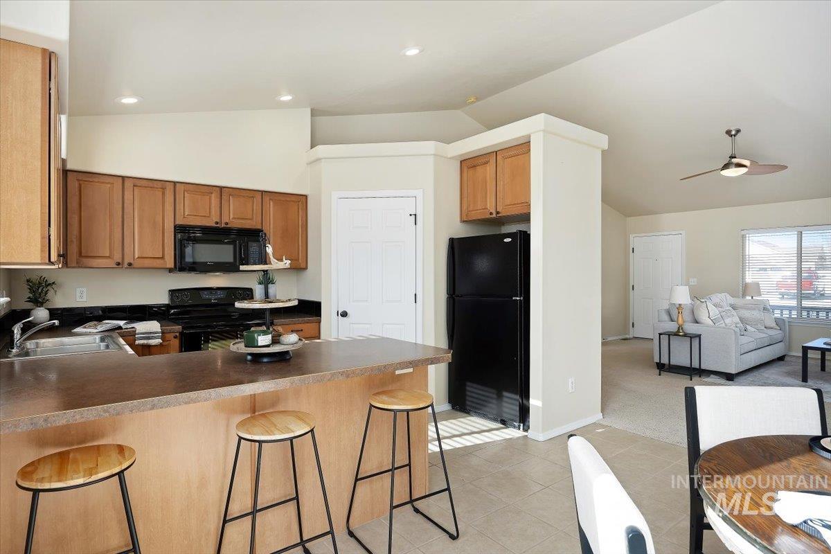 Kitchen featuring lofted ceiling, black appliances, dark countertops, a peninsula, and a breakfast bar