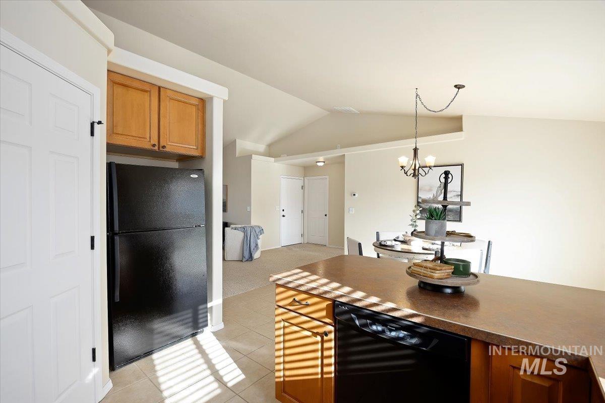 Kitchen featuring brown cabinets, black appliances, light tile patterned flooring, dark countertops, and lofted ceiling