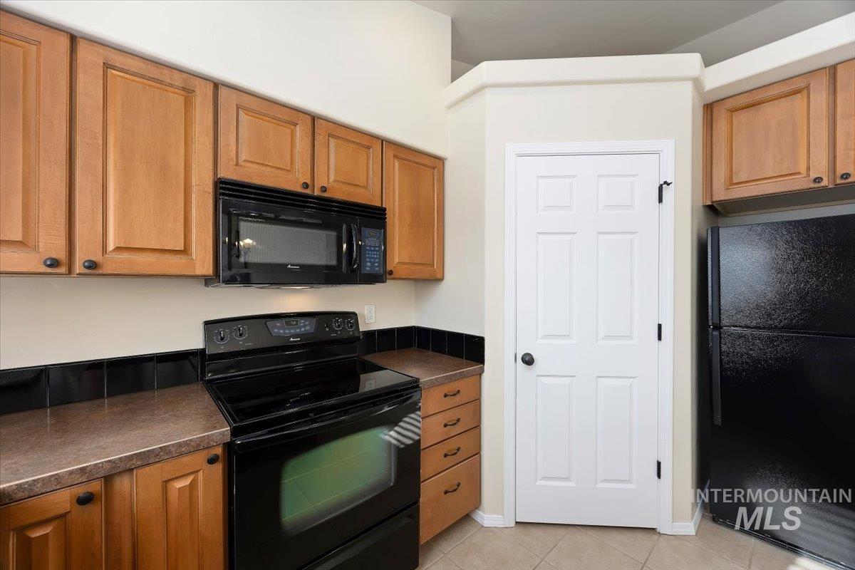Kitchen with black appliances, dark countertops, light tile patterned floors, and brown cabinetry