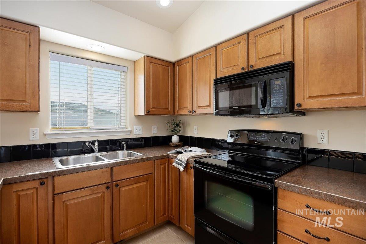 Kitchen featuring dark countertops, black appliances, and brown cabinets