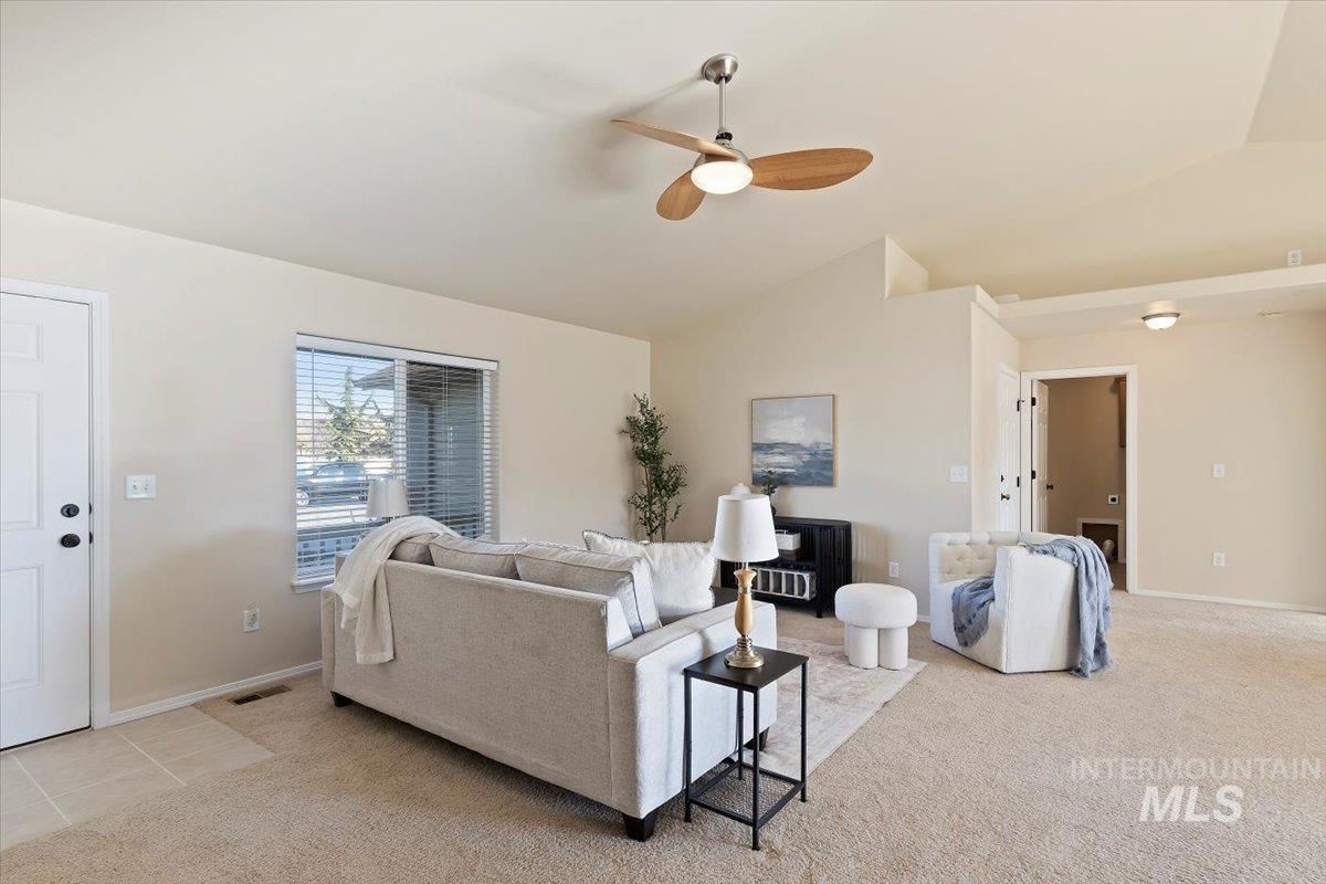 Living room featuring lofted ceiling, a ceiling fan, and light colored carpet