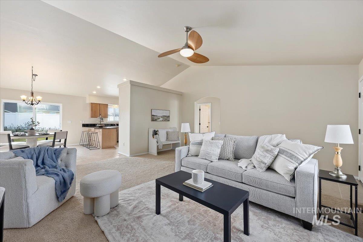 Living area featuring vaulted ceiling, arched walkways, a chandelier, light carpet, and ceiling fan