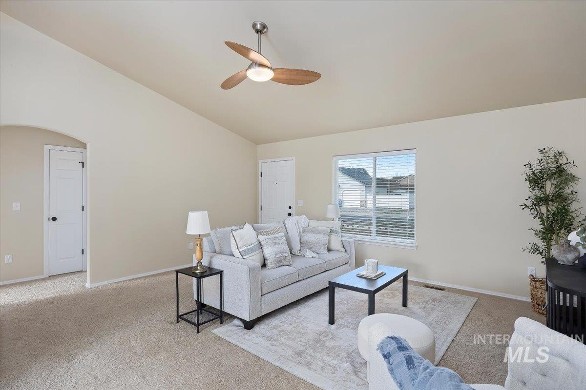 Living room with vaulted ceiling, carpet flooring, arched walkways, and a ceiling fan