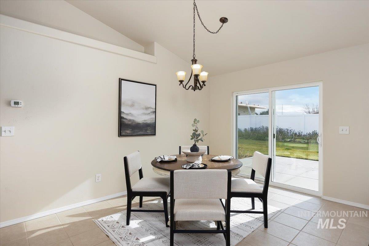 Dining area with light tile patterned flooring, vaulted ceiling, and a chandelier