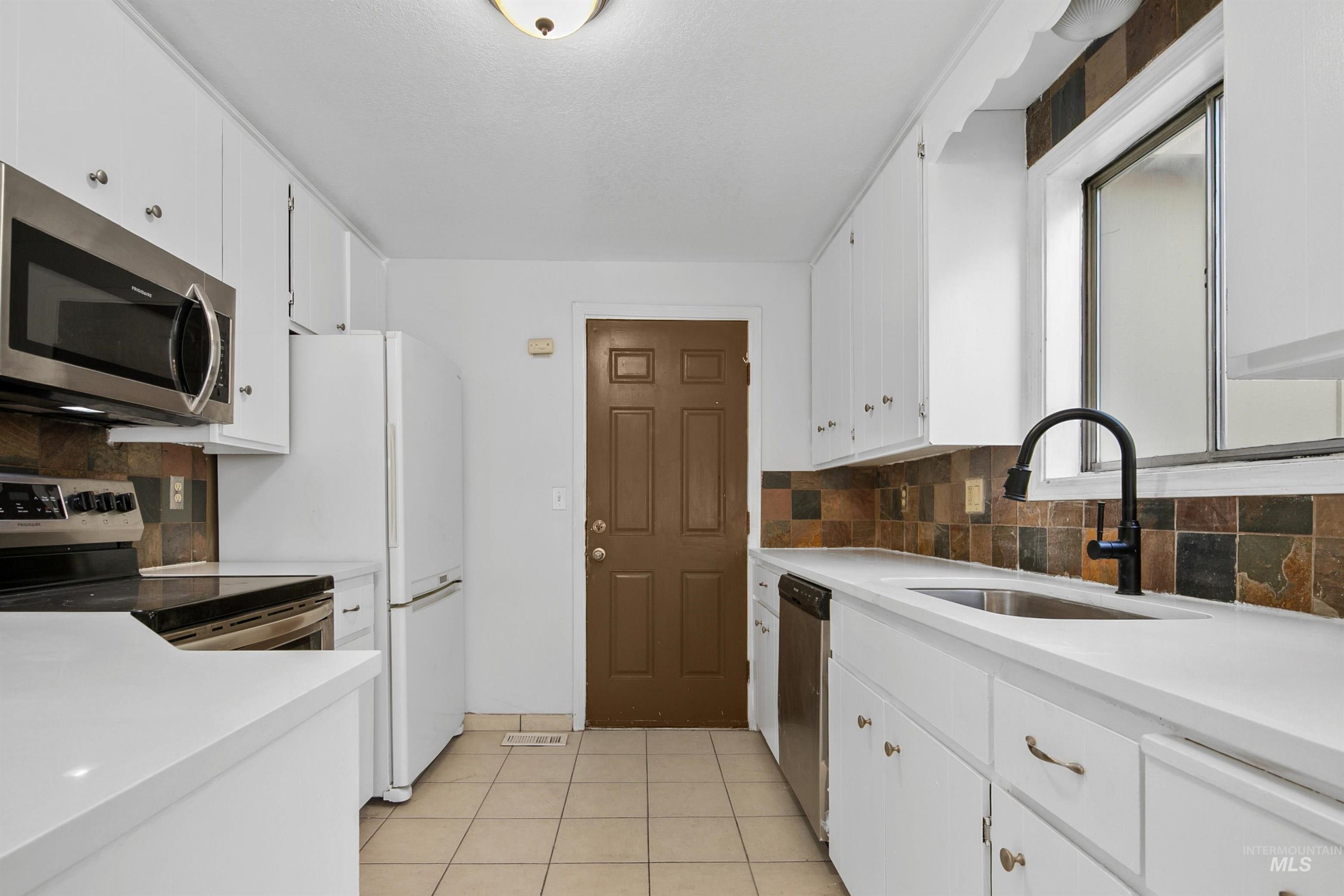 Kitchen featuring stainless steel appliances, white cabinetry, tasteful backsplash, and light tile patterned floors