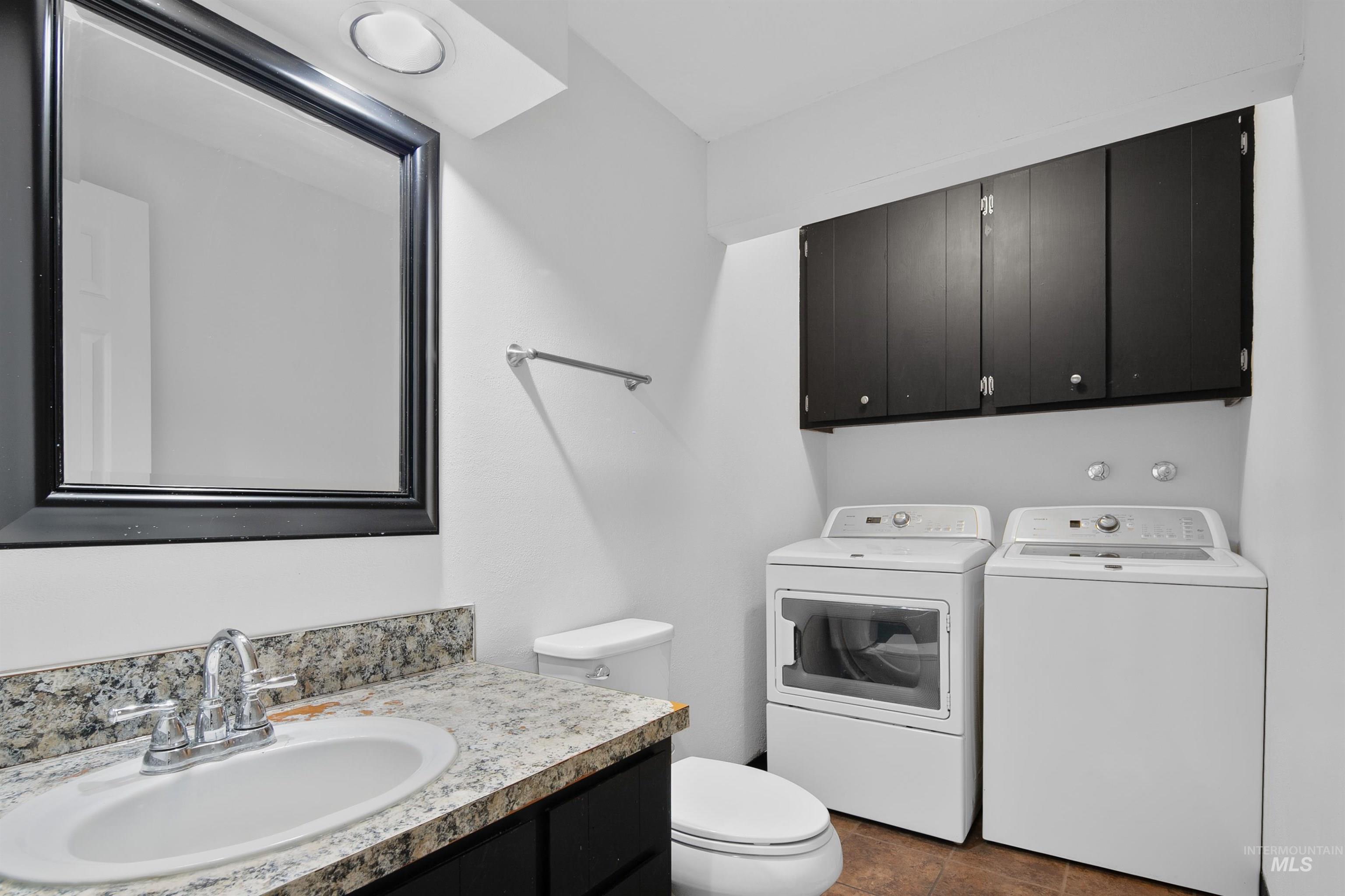 Bathroom featuring washing machine and clothes dryer, vanity, and dark tile patterned flooring
