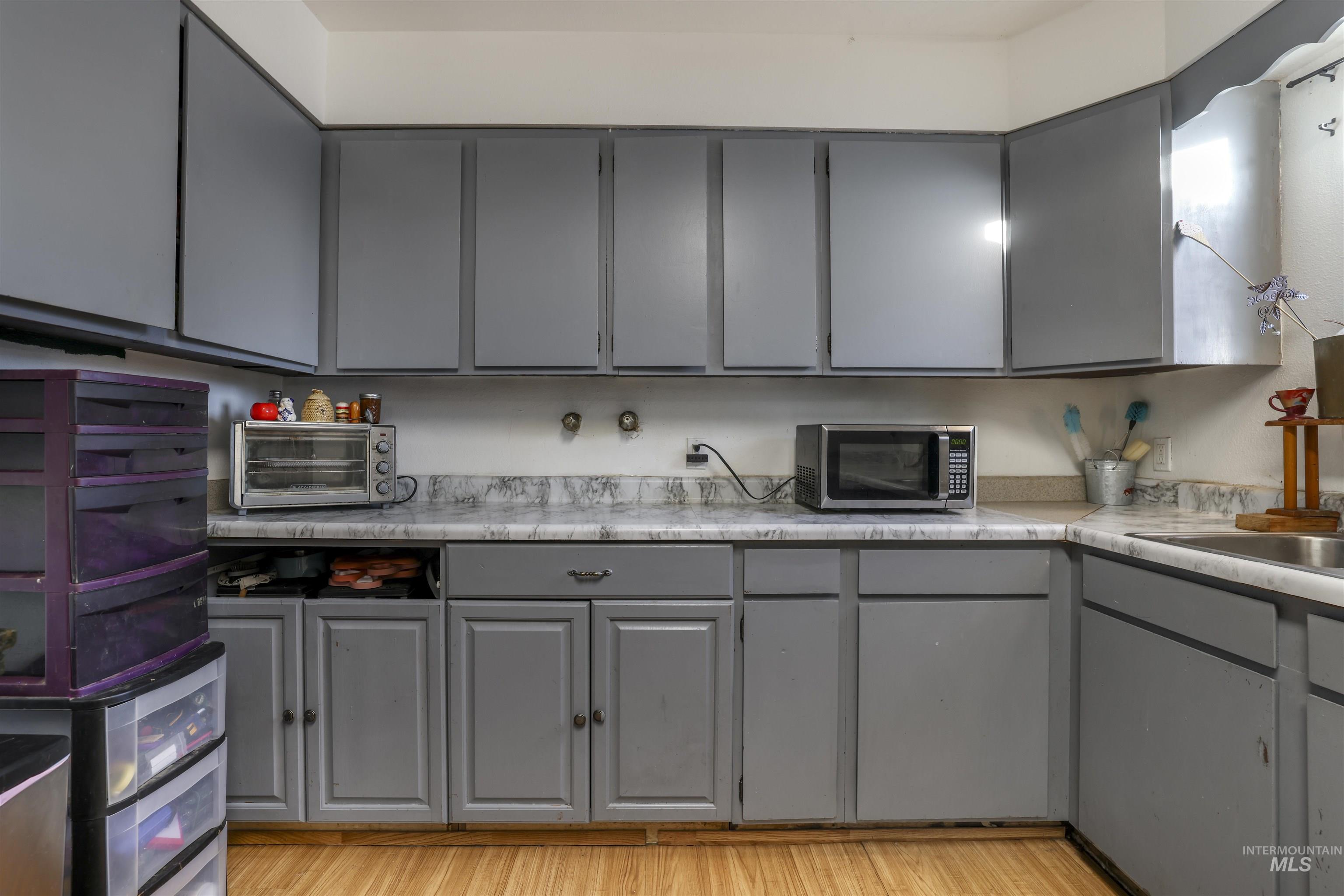 Kitchen featuring gray cabinetry, light countertops, stainless steel microwave, and light wood-style floors