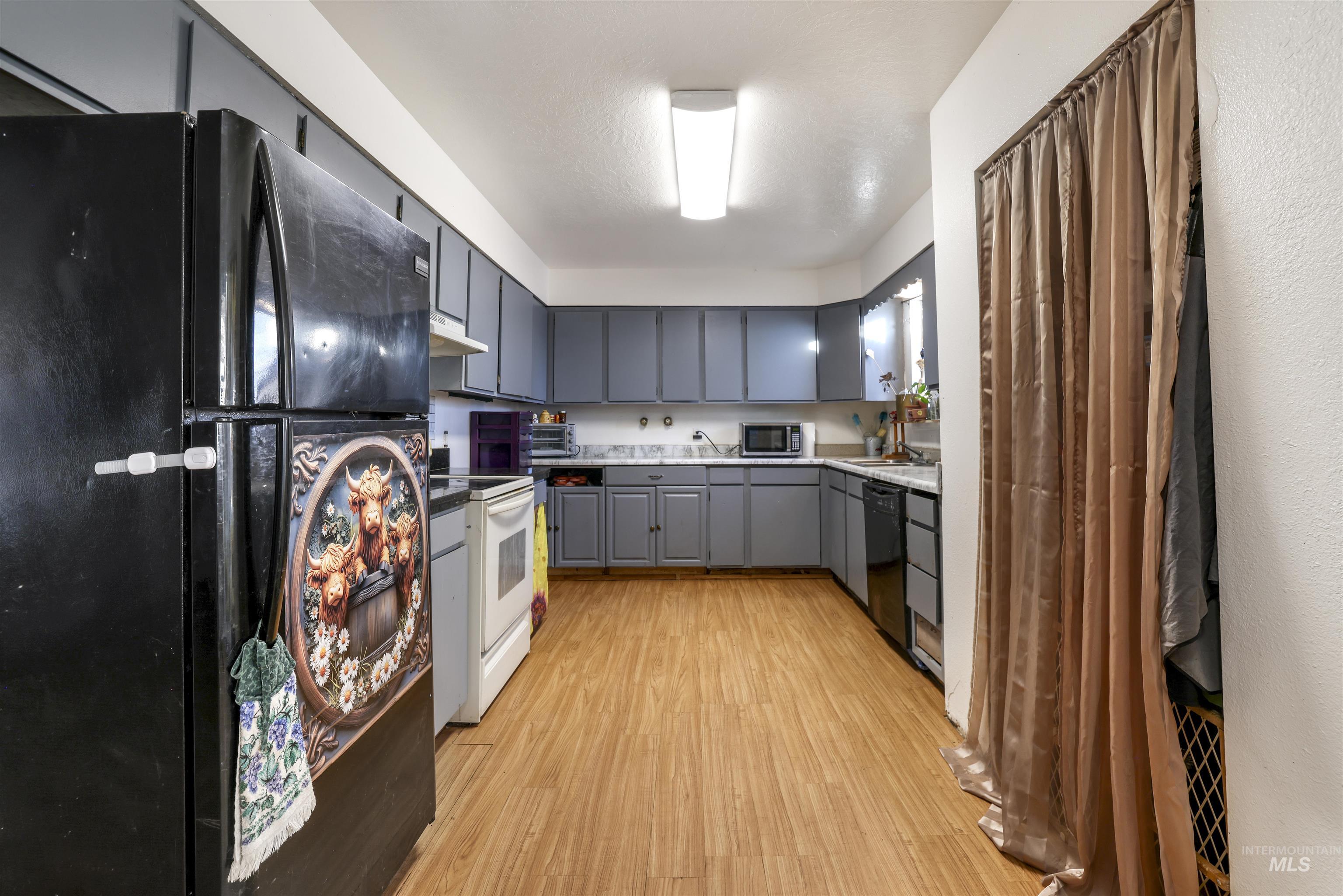 Kitchen with black appliances, light wood finished floors, gray cabinets, light countertops, and under cabinet range hood