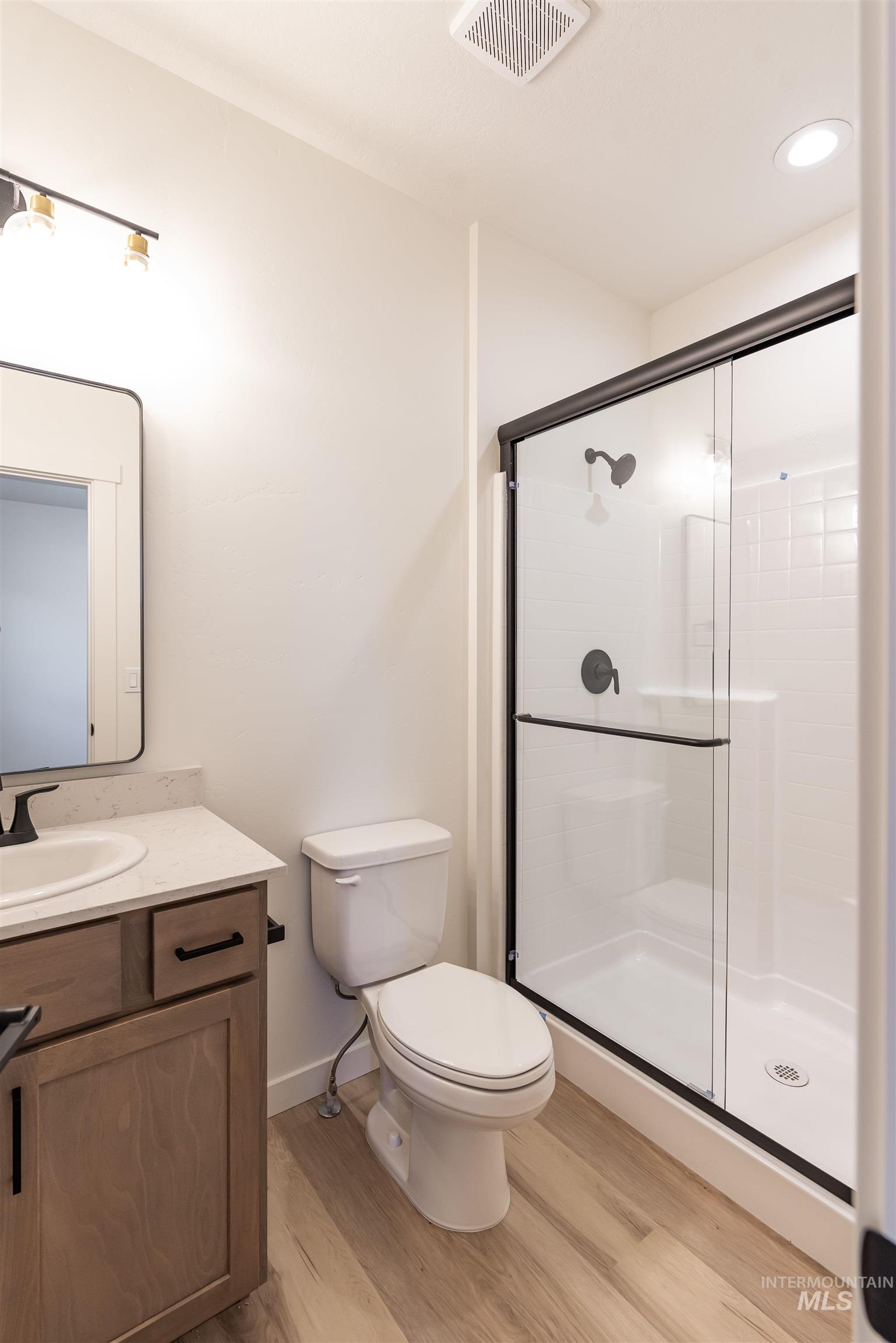 Full bath with vanity, light wood-style flooring, a shower stall, and recessed lighting