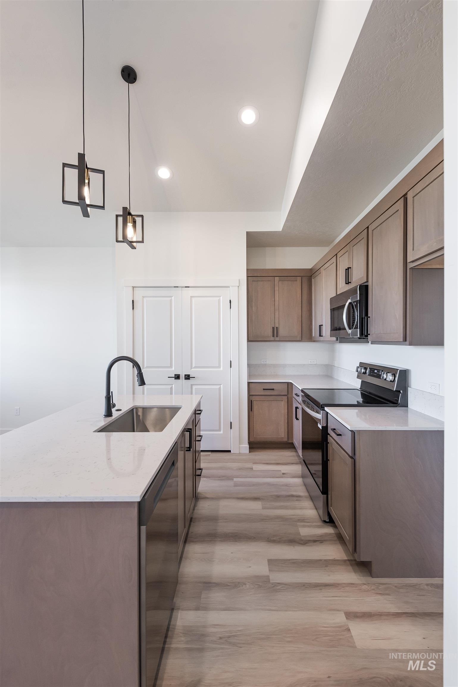 Kitchen featuring appliances with stainless steel finishes, pendant lighting, light stone countertops, light wood-style floors, and a center island with sink