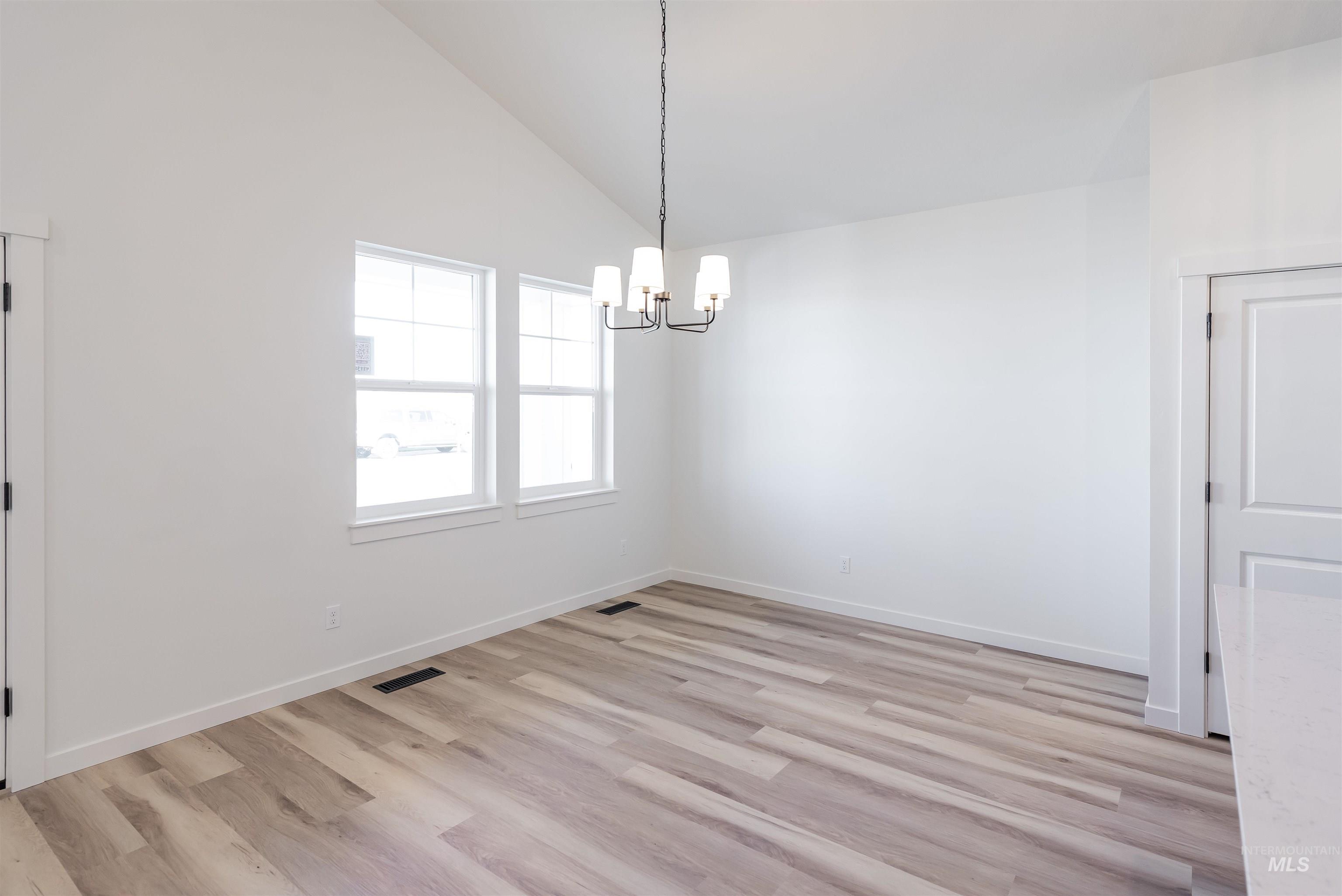 Unfurnished dining area with light wood-type flooring, high vaulted ceiling, and a chandelier
