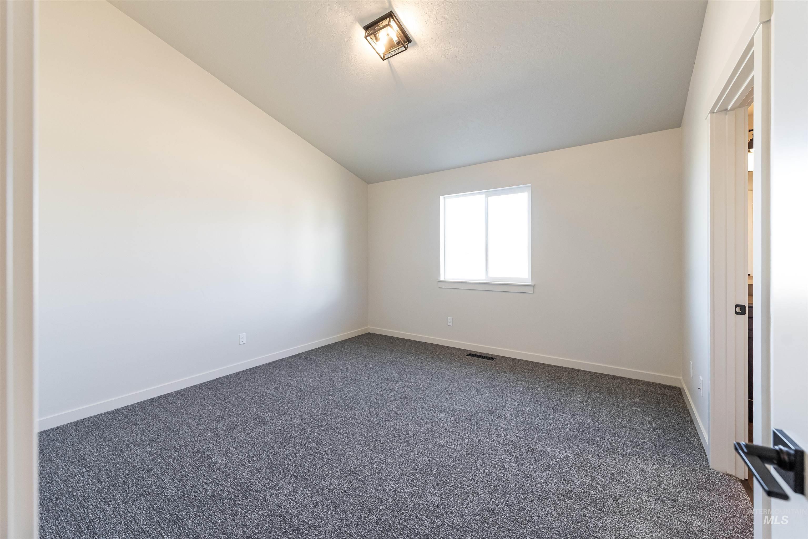 Unfurnished room with vaulted ceiling and dark carpet