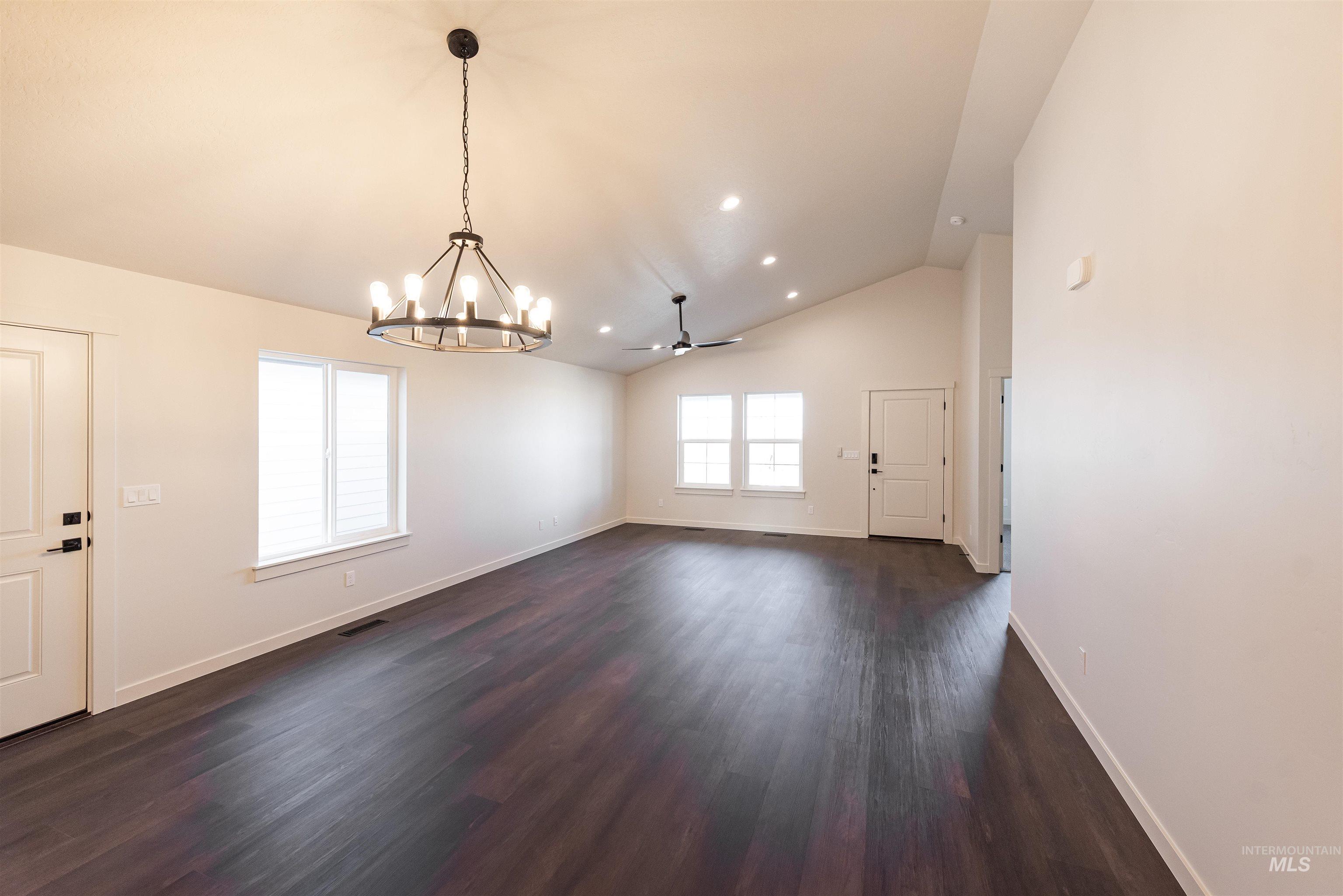 Unfurnished dining area featuring dark wood-type flooring, vaulted ceiling, ceiling fan, recessed lighting, and a chandelier