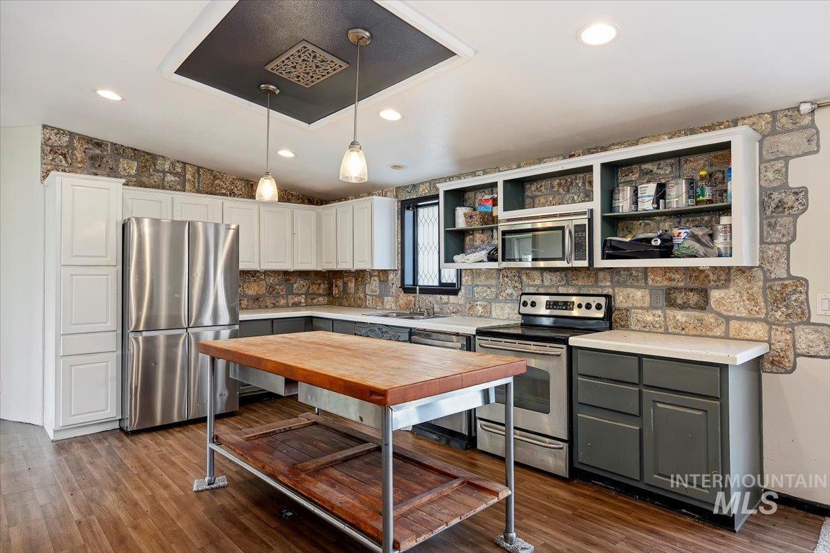 Kitchen with stainless steel appliances, gray cabinets, decorative light fixtures, dark wood-style floors, and recessed lighting