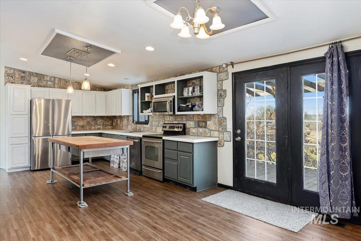 Kitchen with stainless steel appliances, open shelves, hanging light fixtures, white cabinets, and gray cabinetry