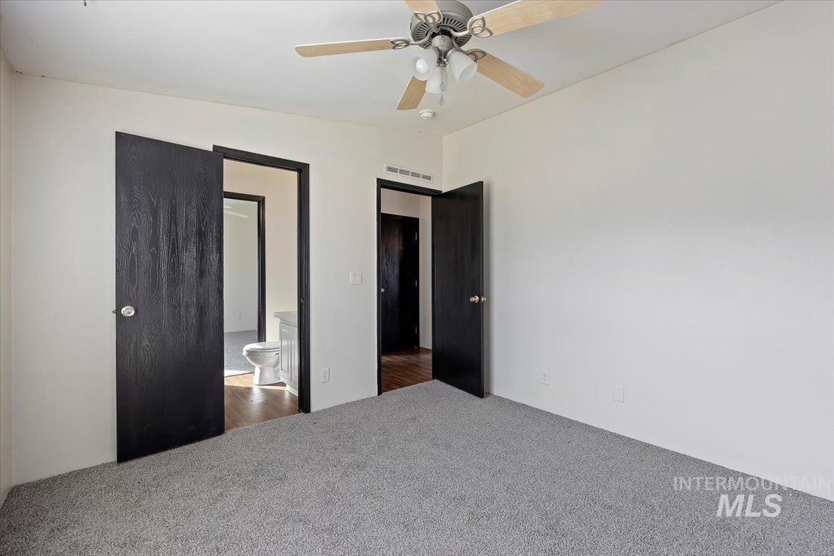 Carpeted bedroom featuring ensuite bath and a ceiling fan