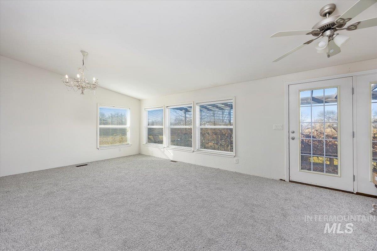 Carpeted spare room with vaulted ceiling, a chandelier, and a ceiling fan