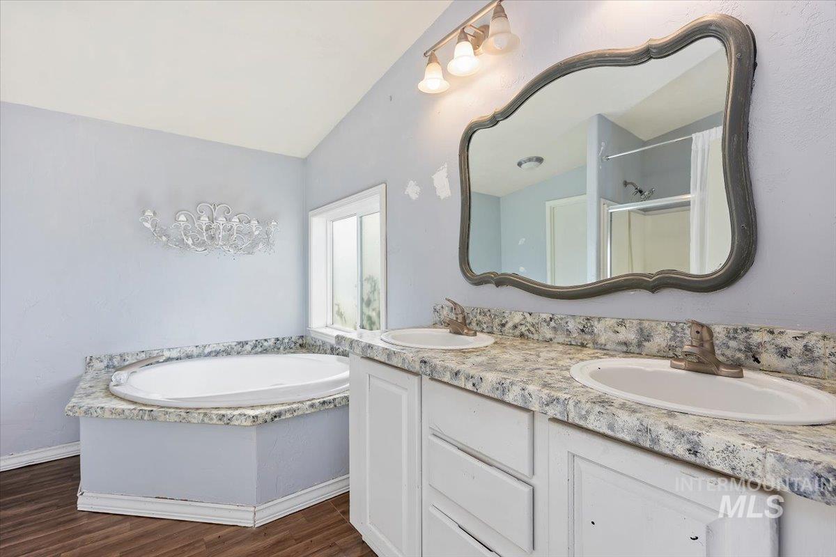 Full bath featuring a bath, a shower stall, double vanity, and dark wood-style floors