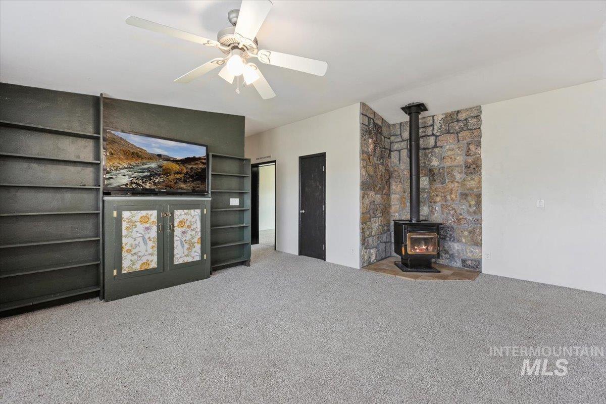 Carpeted living room featuring a wood stove and a ceiling fan
