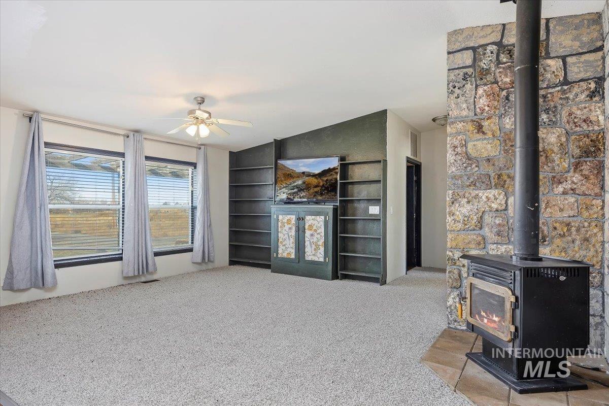 Living area featuring a wood stove, light colored carpet, built in features, and a ceiling fan