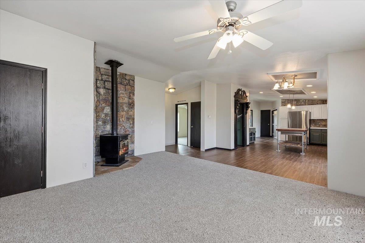 Unfurnished living room with a wood stove, dark colored carpet, dark wood-style flooring, and a ceiling fan