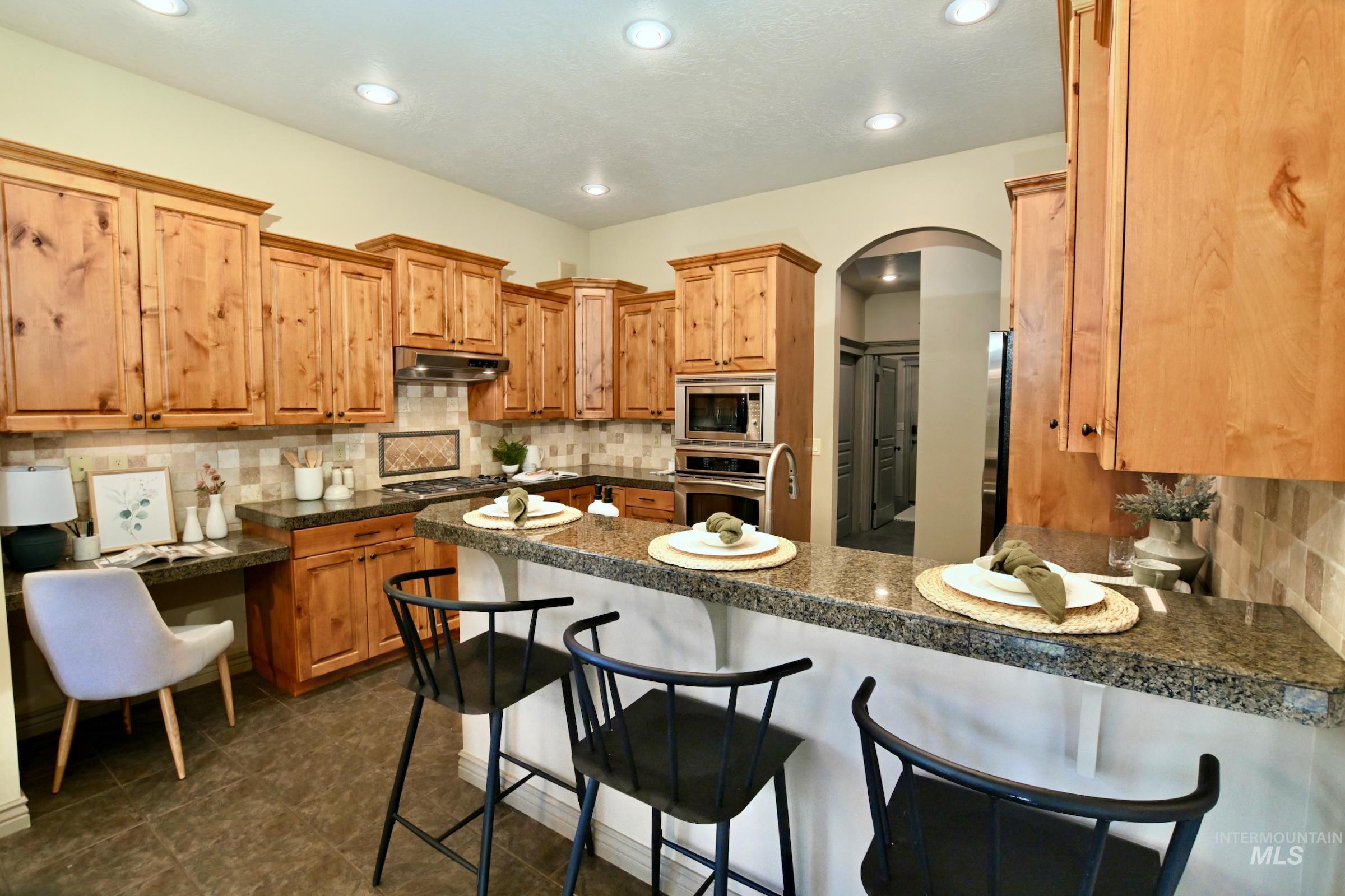 Kitchen with a kitchen breakfast bar, decorative backsplash, a peninsula, arched walkways, and recessed lighting