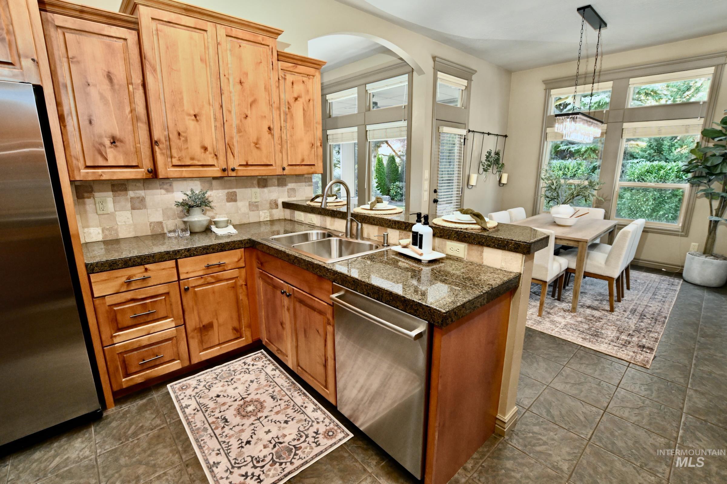Kitchen with tile counters, appliances with stainless steel finishes, backsplash, a peninsula, and decorative light fixtures