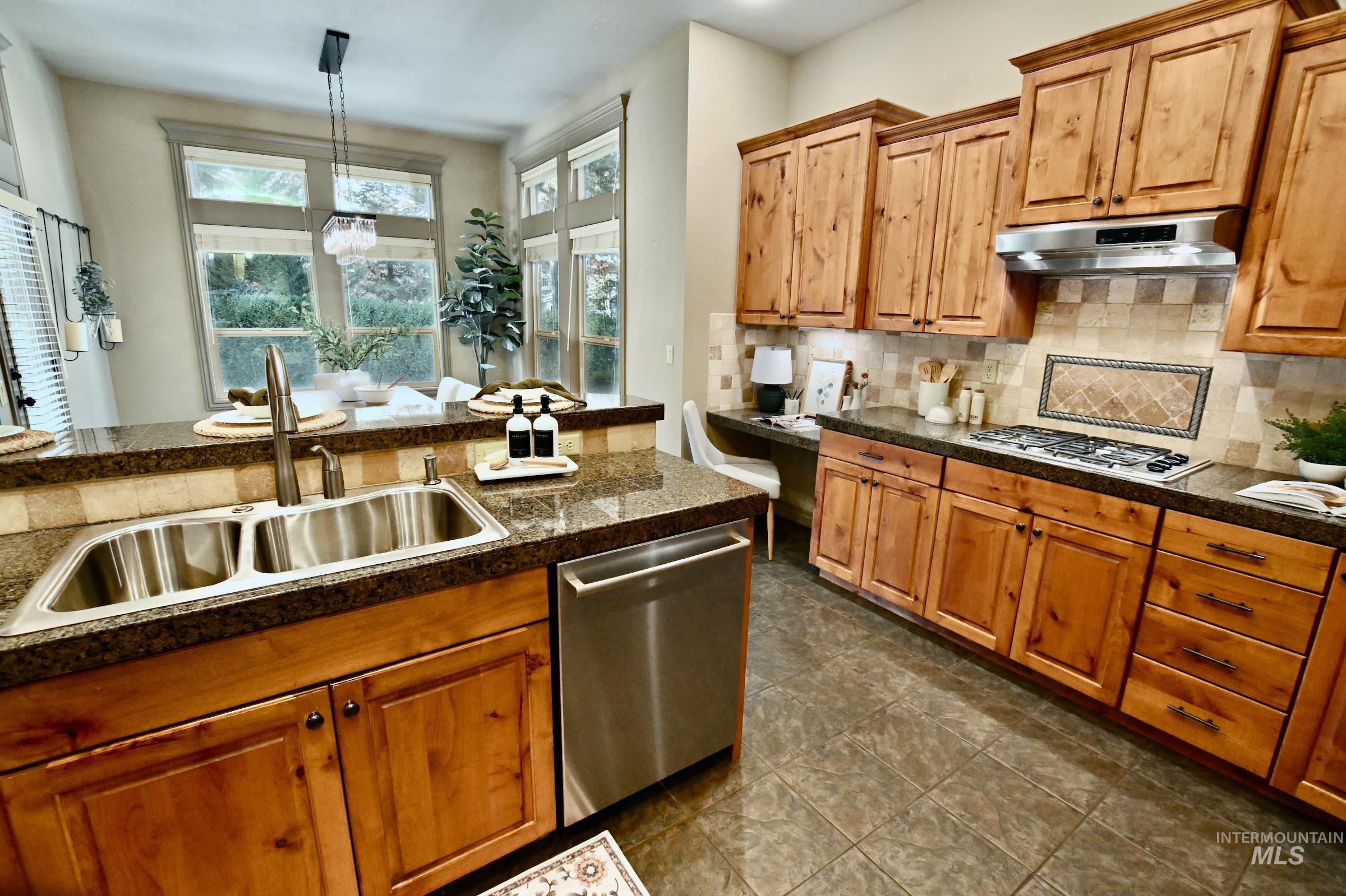 Kitchen featuring appliances with stainless steel finishes, brown cabinetry, tasteful backsplash, and pendant lighting