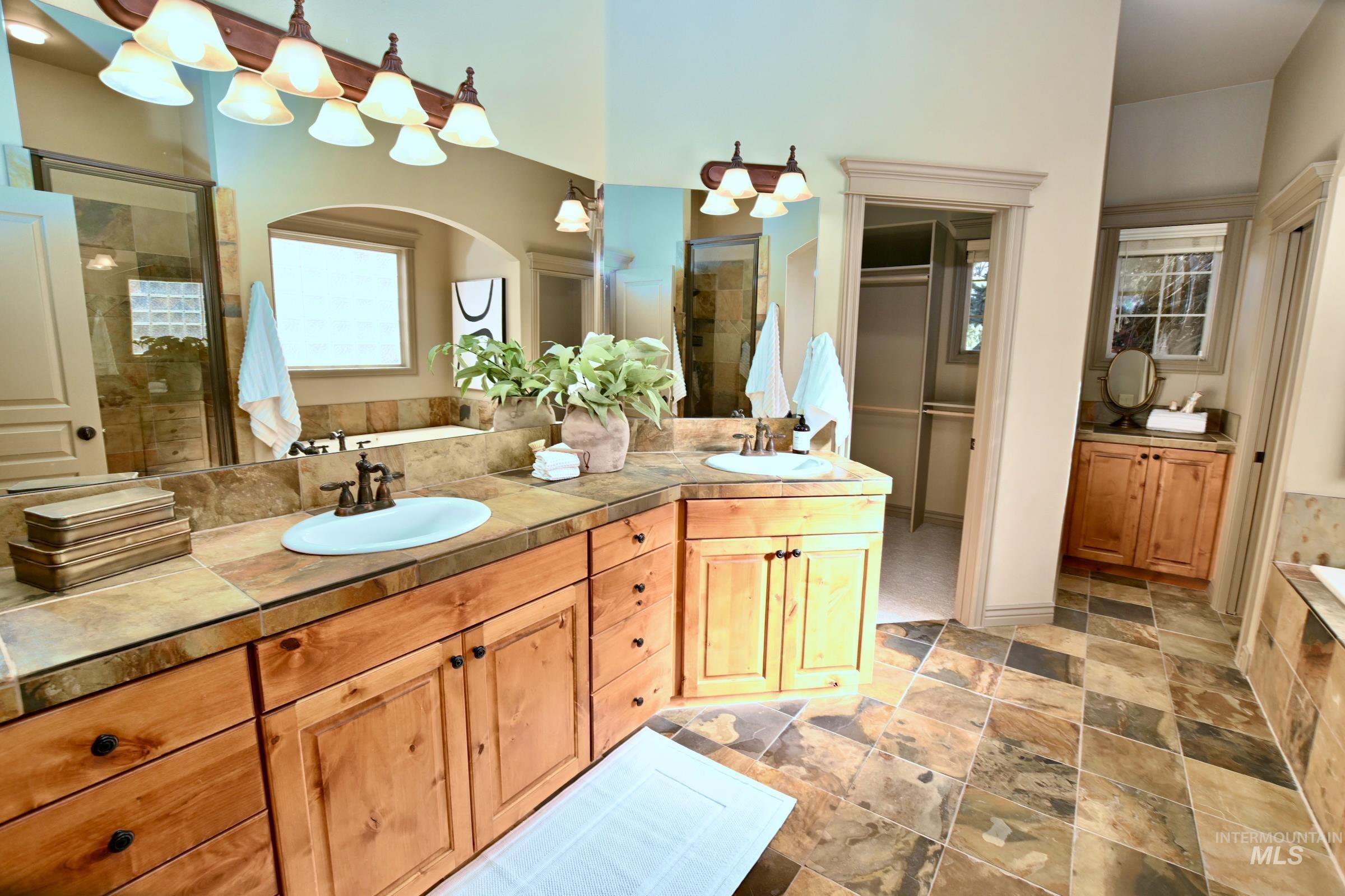 Full bath featuring double vanity, a bath, a stall shower, and stone tile flooring