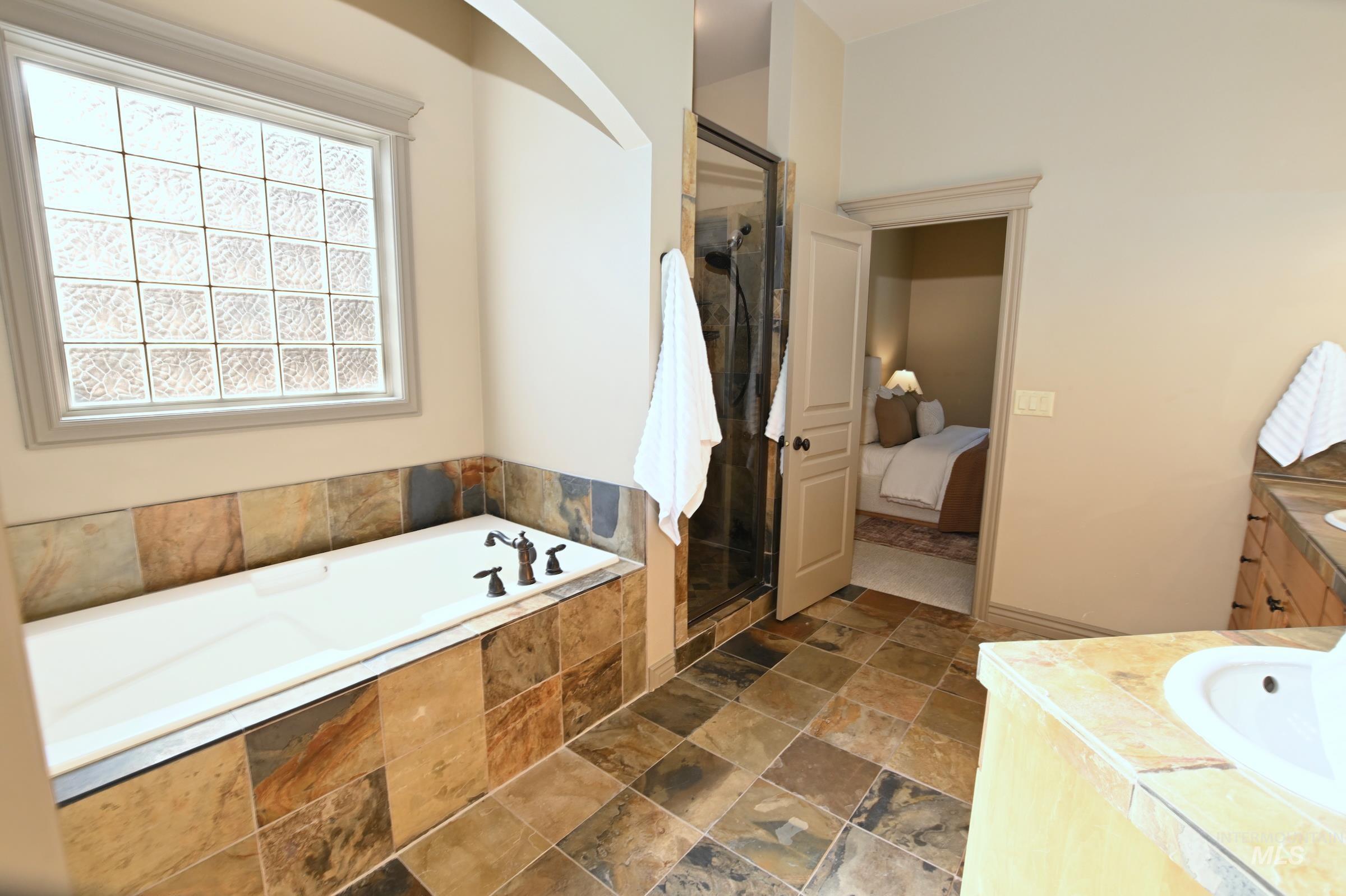 Ensuite bathroom featuring a garden tub, vanity, a shower stall, and stone tile flooring