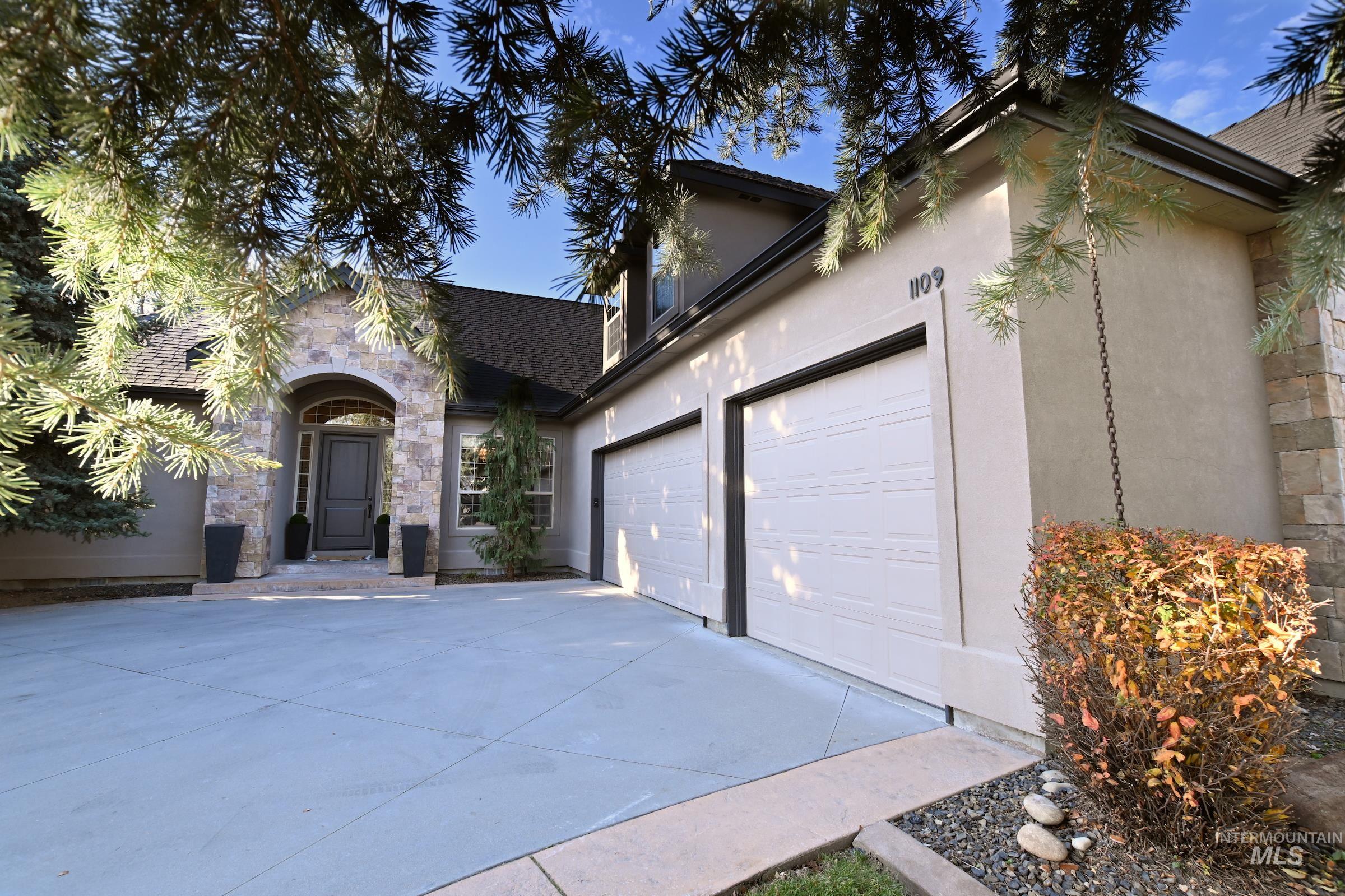 View of front of property featuring an attached garage, stone siding, driveway, and stucco siding