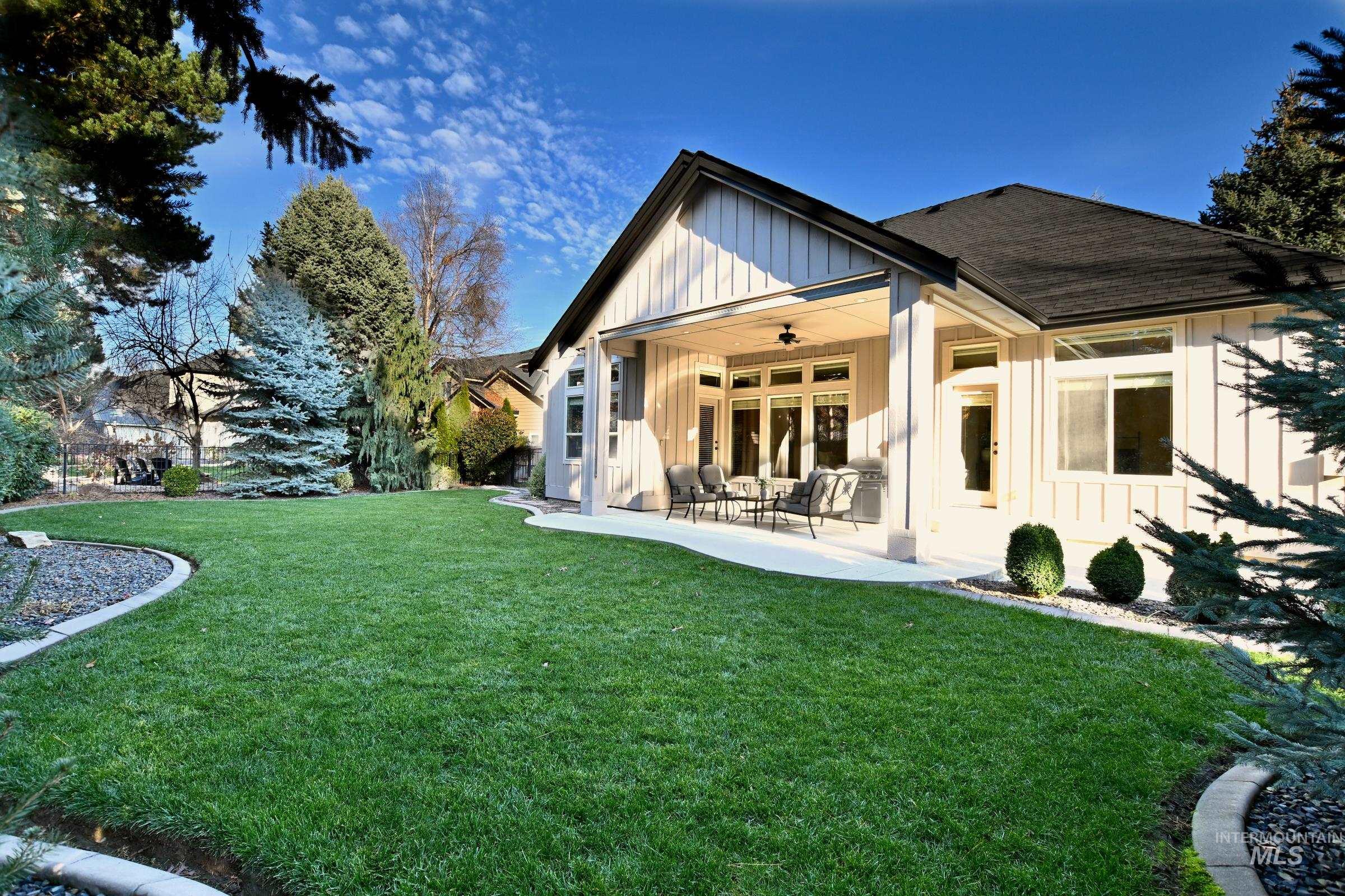 Back of property with board and batten siding, ceiling fan, and a lawn