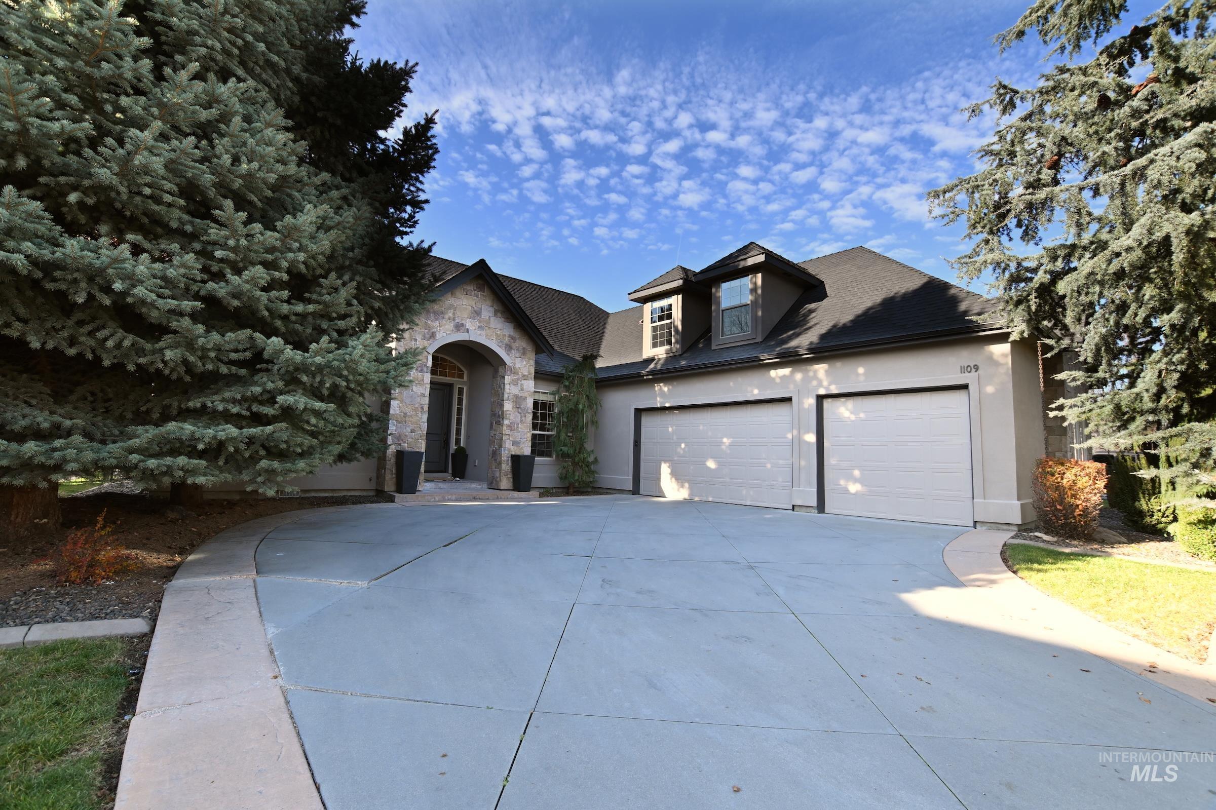 View of front facade with stone siding, driveway, stucco siding, and an attached garage