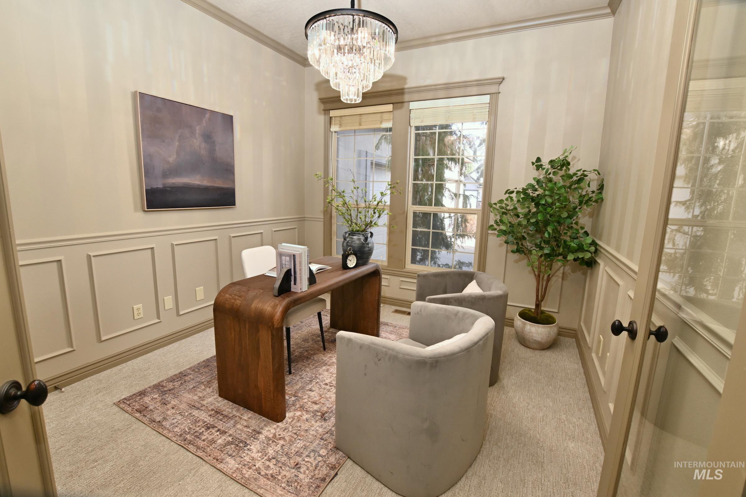 Living area featuring a desk, a decorative wall, light carpet, ornamental molding, and wainscoting