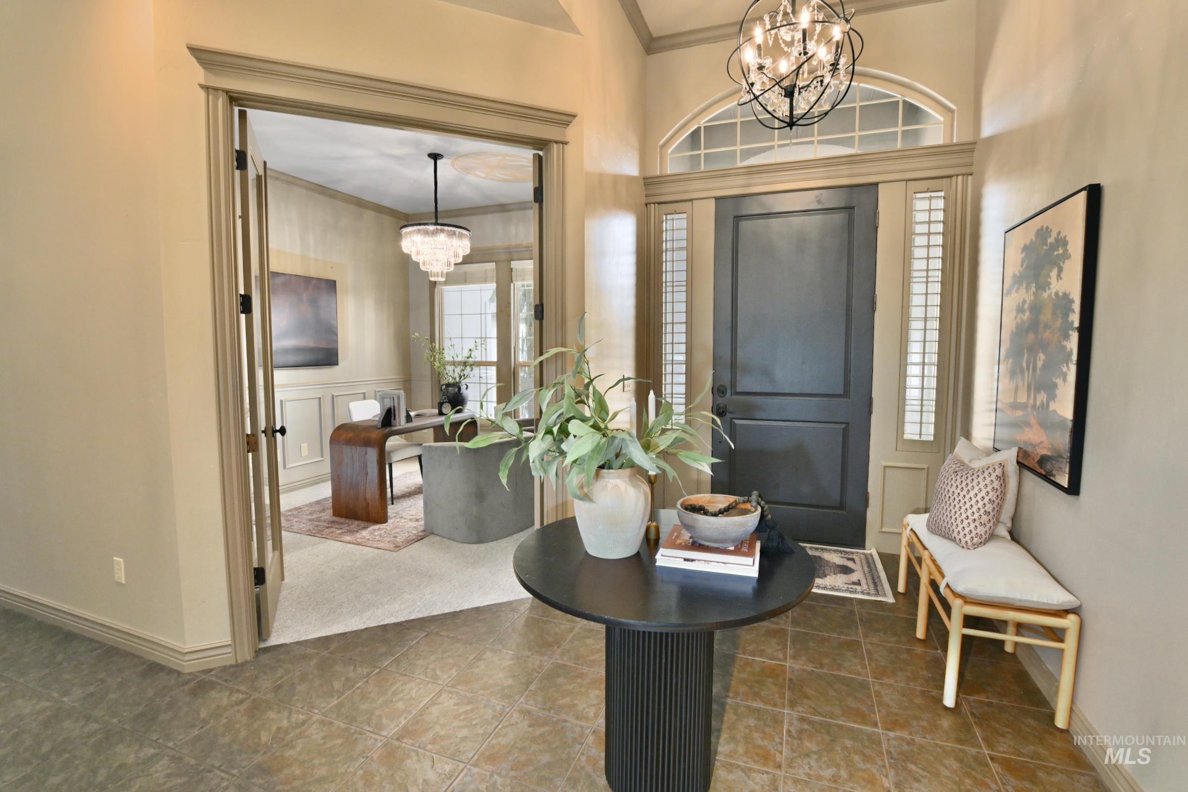 Tiled entryway with a chandelier, ornamental molding, a decorative wall, and a wainscoted wall