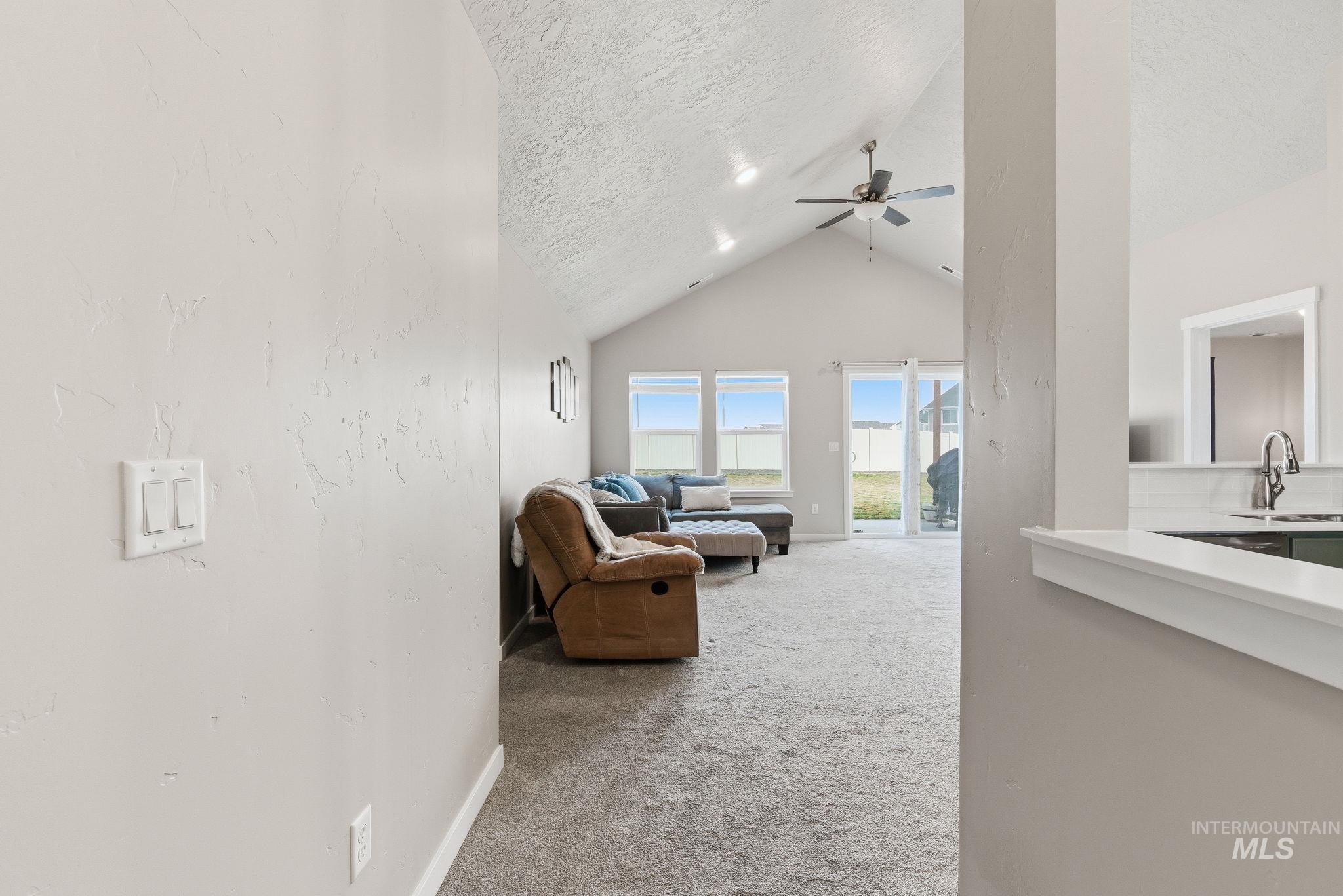 Living room featuring light colored carpet, a textured ceiling, high vaulted ceiling, and ceiling fan
