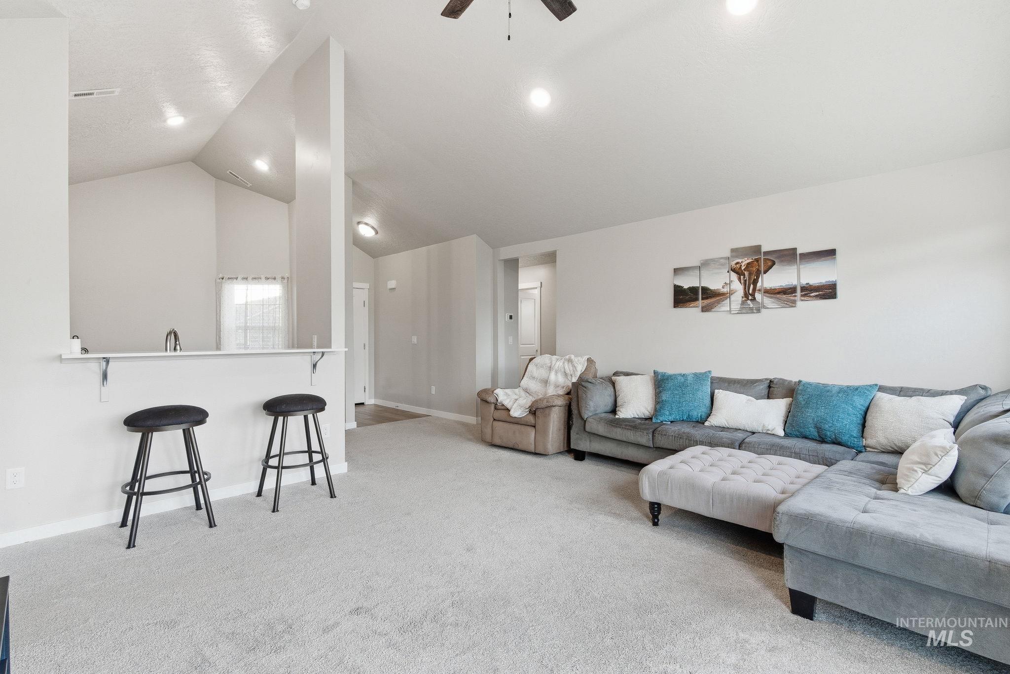 Living area with light colored carpet, ceiling fan, and lofted ceiling